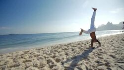 Brazilian martial artist cartwheels and flips backwards across Ipanema Beach in slow motion Stock Footage