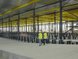 WS PAN two engineers in hi-viz vests walking down ramp  in large hangar, discussing plans; stop at bottom of ramp;  rear view, RED R3D 4K Stock Footage