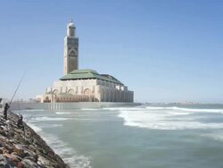 WS T/L  Side view of World's third largest mosque of Hassan II and mens doing fishing near sea shore / Casablanca, Morocco Stock Footage