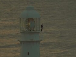 MS AERIAL TS Top shot of lighthouse and ocean at sunset and keeper standing on platform Stock Footage