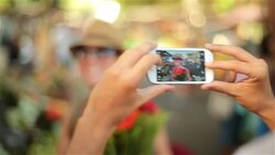Cute girl smiles for smartphone photo with bouquet of flowers in sunny Brazilian market Stock Footage