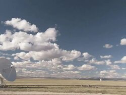 Long Shot zoom-out - Clouds drift above an array of satellite dishes in a field / New Mexico, USA Stock Footage