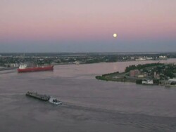 Wide Shot High Angle - Boat glides down calm river near town at dusk / New Orleans Louisiana Stock Footage
