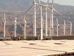 PAN with freight train across solar photovoltaic power plant next to wind farm and interstate highway traffic  / Palm Springs, California, USA Stock Footage