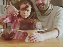 CU TU Shot of daddy and daughter sitting at kitchen table adding chocolate icing to cake / London, United Kingdom  Stock Footage