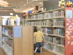 WS PAN young mother with two small children enter kids section in public library filled with childrens books / Rancho Mirage, California, USA Stock Footage