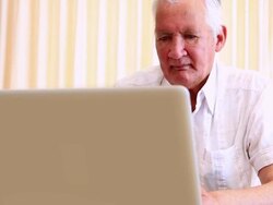 Senior man sitting at table using laptop Stock Footage