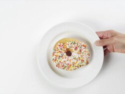 CU Woman hand entering setting down round white plate with large donut with white frosting and colorful sugar sprinkles / Omaha, Nebraska, United States Stock Footage
