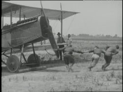 Three men spin the propeller on a biplane. News Clip