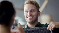 Laughing man holds up sweater and poses for smartphone photo in trendy clothing shop Stock Footage