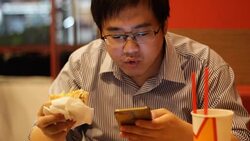 man using smartphone while eating hamburger Stock Footage