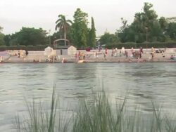 PAN People sitting and standing along the opposite bank of the Ganges river / Kashi, Uttar Pradesh, India Stock Footage
