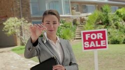 Portrait of smiling realtor holding keys in front of house with For Sale sign Stock Footage