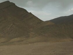 Panning shot of dark coloured mountains, leading down to a desolate and dry river bed. Stock Footage