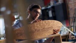 Young artisan polishes wooden skateboard with cloth in workshop Stock Footage