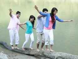 Group of friends walking on a fallen tree at riverbank Stock Footage