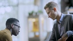 Clothing store clerk chats with customer while tying his shoelaces Stock Footage