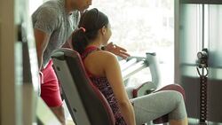 Personal trainer guiding woman doing thigh squeezes on machine at gym Stock Footage