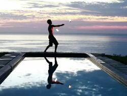 WS Male poi dancer without shirt performing with fireballs in front of pool with reflection of his silhouette in pool at sunrise / Montezuma, Costa Rica Stock Footage