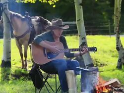 Cowgirl playing Guitar around campfire with horse Stock Footage
