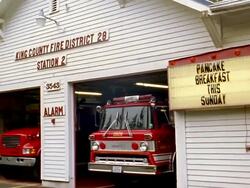 Medium shot pan fire station w/parked fire trucks and flashing sign 'pancake breakfast this Sunday' Stock Footage