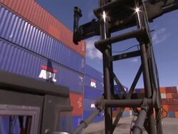 A driver steers a crane past a row of shipping containers. Stock Footage