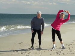 WS Mature couple stretching before run on beach / Sea Bright, New Jersey, USA Stock Footage