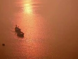 Two boats move slowly across reflection of evening sun shimmering like copper on wide expanse of river.  India Stock Footage