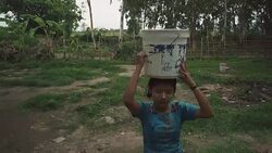 W/S-M/S STEADYCAM frontshot, Burmese teenage girl carrying water to her house in a rural area Stock Footage