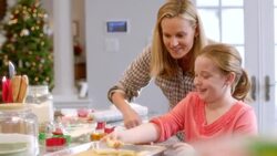 Happy mother helps daughter place Christmas tree-shaped cookie dough on baking sheet Stock Footage