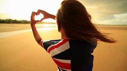 Female on beach makes heart shape finger frame, Australian flag Stock Footage