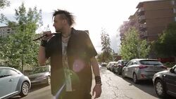 Cool young man with mohawk holding guitar over shoulder standing in sunny urban street Stock Footage