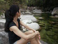 MS, Woman sitting on large boulder in riverbed in tropical rainforest,  Mossman, Queensland, Australia Stock Footage