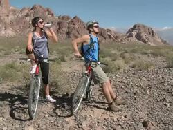 Couple with mountain bikes in rocky terrain, drinking from bottle Stock Footage