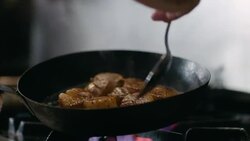 In restaurant kitchen, chef spoons grease over sizzling scallops in iron skillet in slow motion Stock Footage