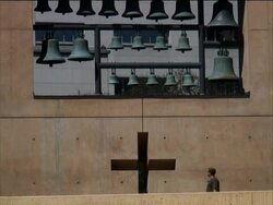Crossing Left: Man Walks Past Giant Cross and Bells Stock Footage