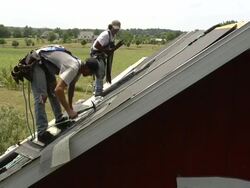 MS Shot of one worker moving shingles while another is hammering on roof of red building / Chelsea, Michigan, United States Stock Footage