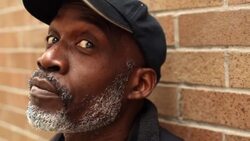 Old man looks up at sky and turns to face camera on urban street corner Stock Footage