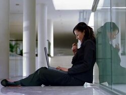 Medium shot businesswoman sitting against wall and typing on laptop Stock Footage