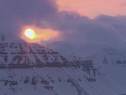 LA Clouds slowly enshrouding the sun as it's peeking over a snow-covered mountaintop / Svalbard, Norway Stock Footage
