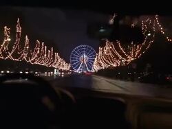 Wide shot car point of view street lined with lighted trees with view of ferris wheel and Luxor obelisk at night / Paris Stock Footage