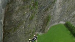 BASE jumper descends from high concrete dam to valley below Stock Footage