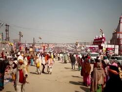 Indian flags fly above festive Kumbh Mela highway with milling crowds of pilgrims, vehicles and hoarding as far as the eye can see.  India Stock Footage