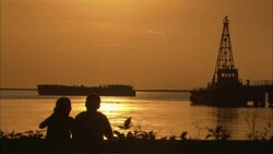 A couple in silhouette watch from shore as a barge passes near a drilling platform. Stock Footage