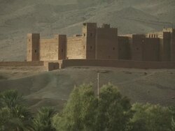 A castle like building stands at the foothills of the a mountain range, surrounded by harsh and dusty terrain. Stock Footage
