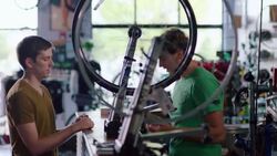 Bike shop mechanic chats with customer while bicycle wheel spins on truing stand Stock Footage