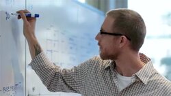 Young businessman writes on conference-room white-board (dolly shot) Stock Footage