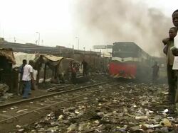 MS PAN Shot of train track running through shanty town and burning plastic with people standing / Lagos, Nigeria Stock Footage