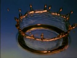 High Speed BCU golden coloured water drop splashing into blue water, high angle Stock Footage