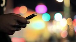 A young Black man standing on a busy city street at night sends a text message. Stock Footage
